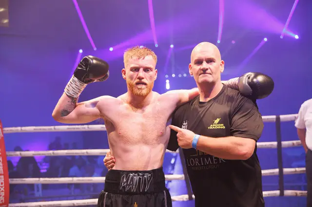 Matthew flexing next to his cornerman under purple ring lights