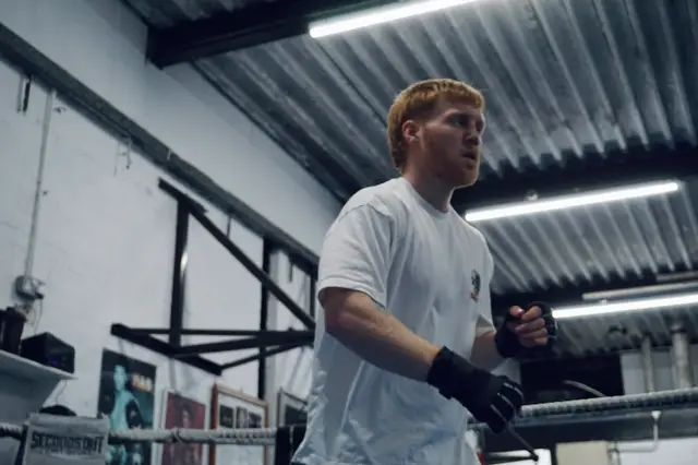 Matthew in the gym in a white T-shirt and bag gloves